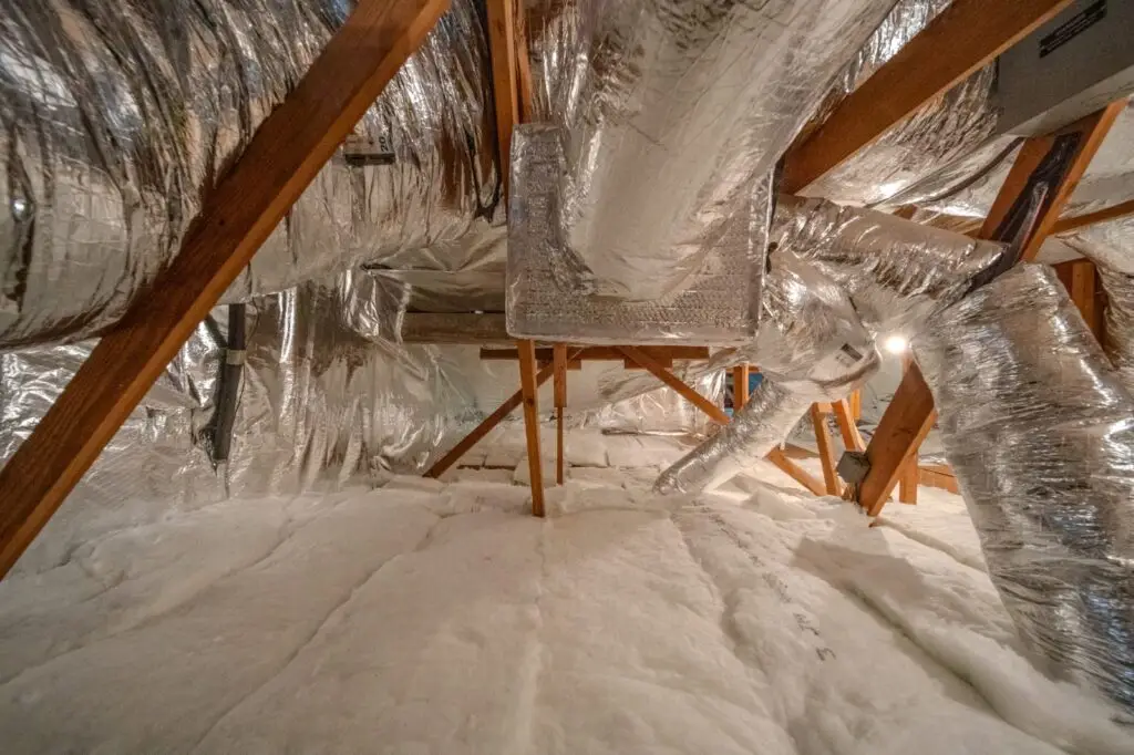 Residential attic crawl space featuring shiny silver radiant barrier foil insulation and blown-in insulation.