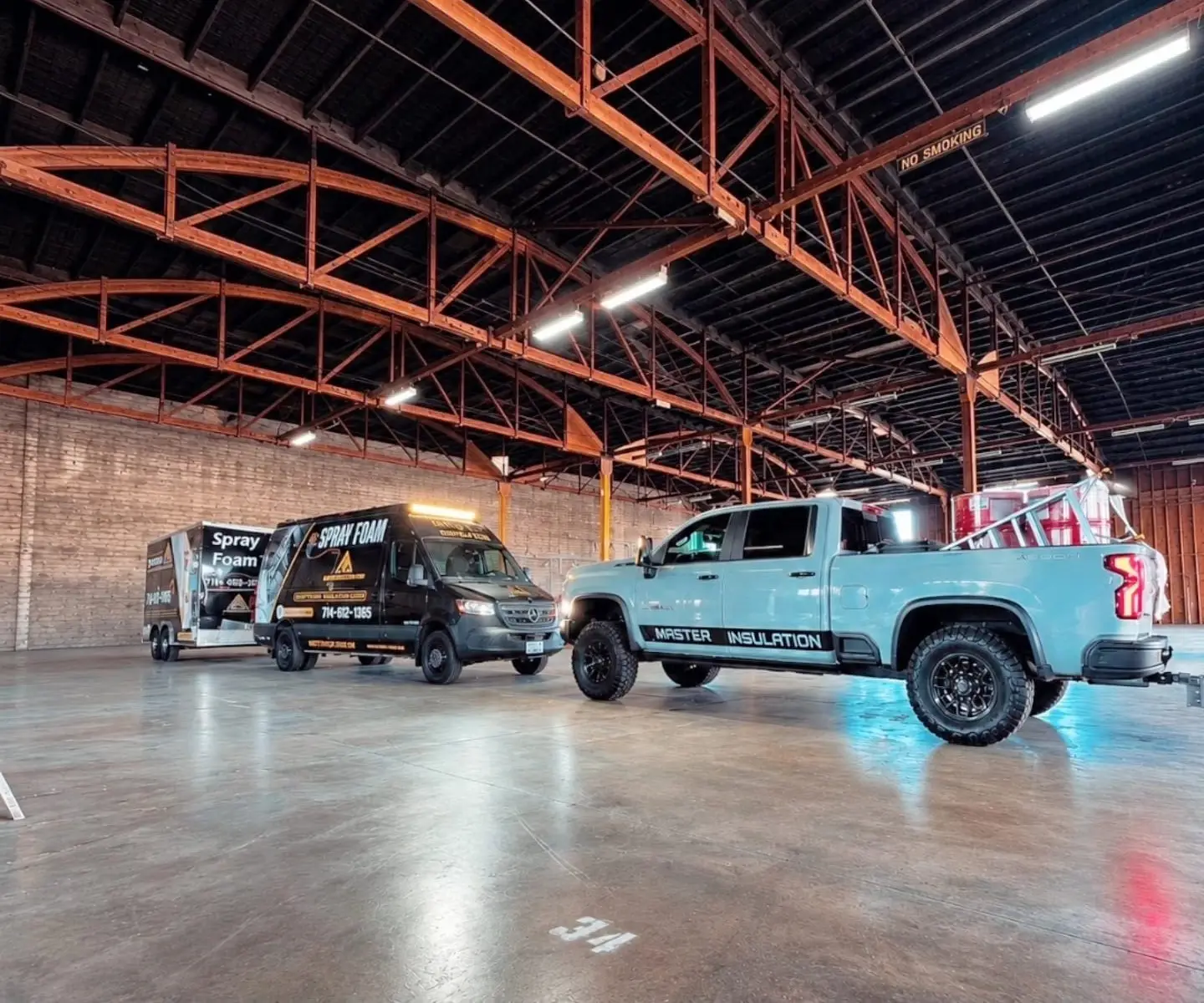 Commercial work trucks and trailers from Master Insulation Corp parked inside a large commercial warehouse in Riverside.