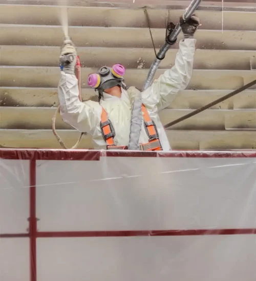 Master Insulation Corp contractor in a full protective suit and respirator applying spray foam insulation to a commercial roof deck.